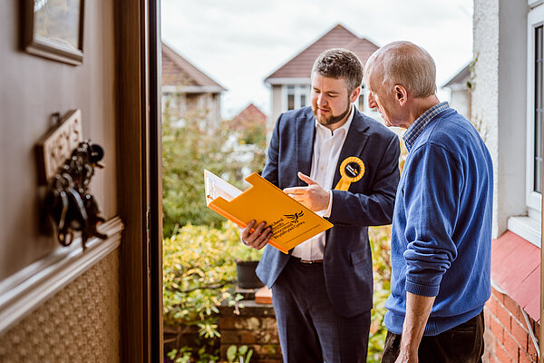 Volunteer speaking to voter on the doorstep, with yellow Lib Dem folder. 