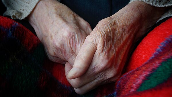 An elderly person's hands clasped together over a blanket