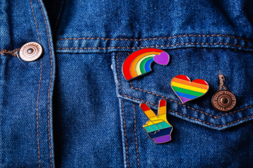 A close crop of a denim jacket with multiple LGBT flag and pride related pins.